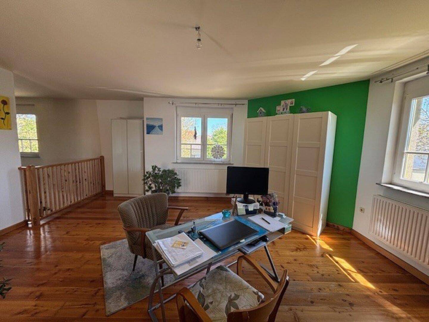 Helles Arbeitszimmer im Obergeschoss mit Holzfußboden, Schreibtisch und Blick ins Grüne.