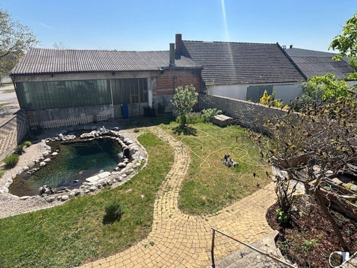 Garten mit Teich, gepflastertem Weg und Blick auf die umliegenden Gebäude.