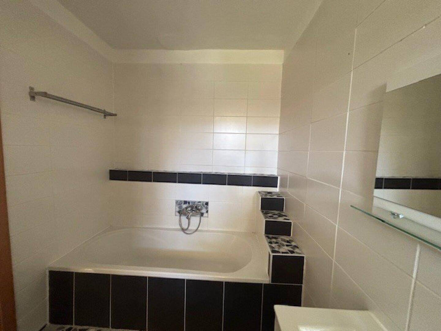 Badezimmer mit Badewanne und weißen Fliesen in schlichtem Design.