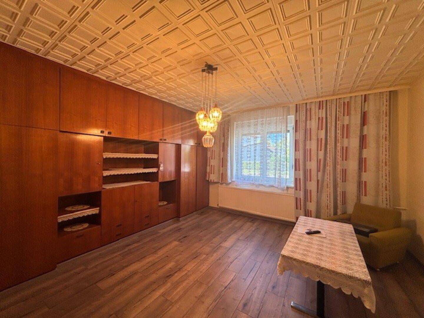 Wohnraum mit großen Holzschränken, strukturiertem Deckenmuster und Fenster mit Vorhängen.
