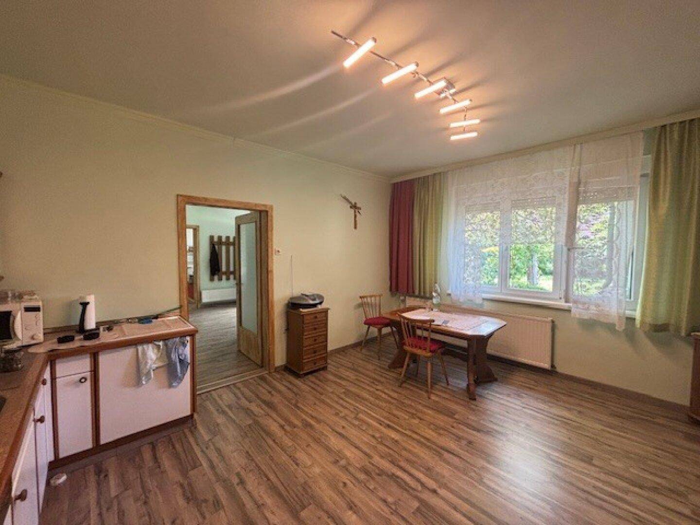 Helle Küche mit Essbereich, Holzoptikboden und Fenster mit Blick in den Garten.