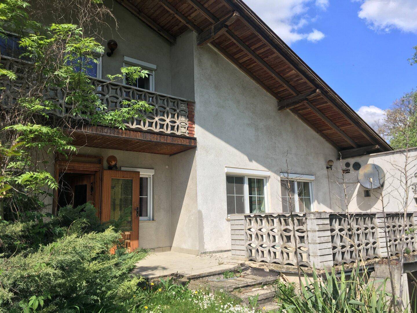 Hausfassade mit Balkon und kleiner Terrasse, beide mit dekorativen Betonbrüstungen.