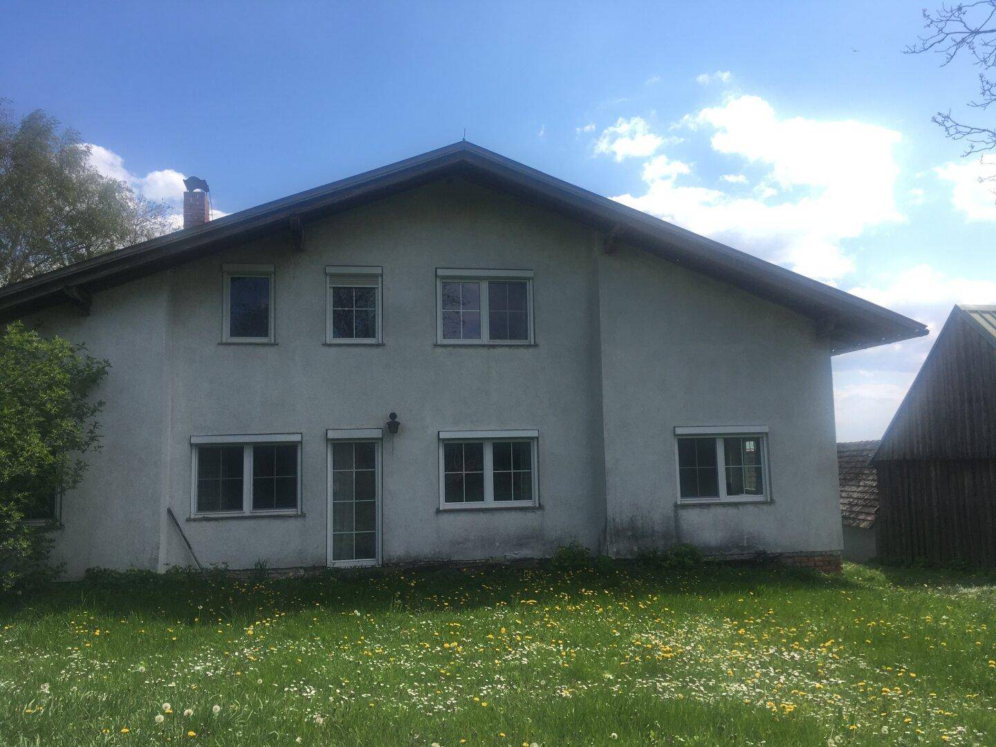 Rückseite des Hauses mit großer Rasenfläche und blühenden Wiesenblumen.