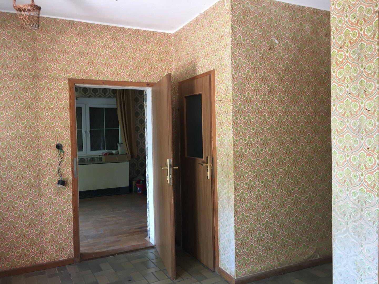 Innenraum mit auffälliger gemusterter Tapete und zwei Holztüren, die zu weiteren Räumen führen.