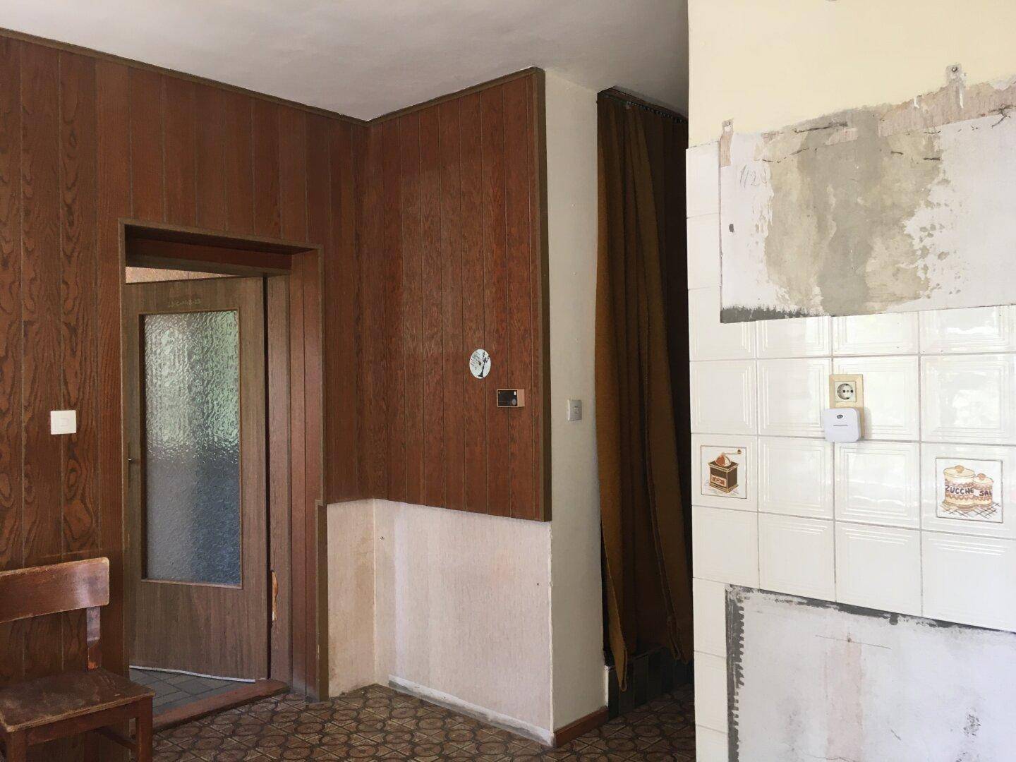 Alte Küche mit Holzvertäfelung und gefliesten Wänden, die Renovierung benötigt.