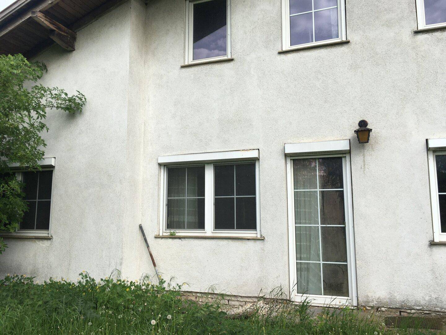 Fassade eines Wohnhauses mit mehreren Fenstern, Rollläden und einer Außentür.