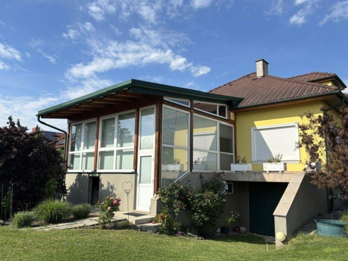 Rückseite des Hauses mit Wintergarten, Gartenzugang und gepflegter Bepflanzung.
