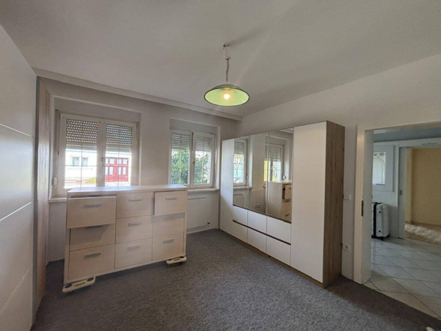 Schlafzimmer mit Teppichboden, großem Spiegelschrank und Fenster mit Rollläden.