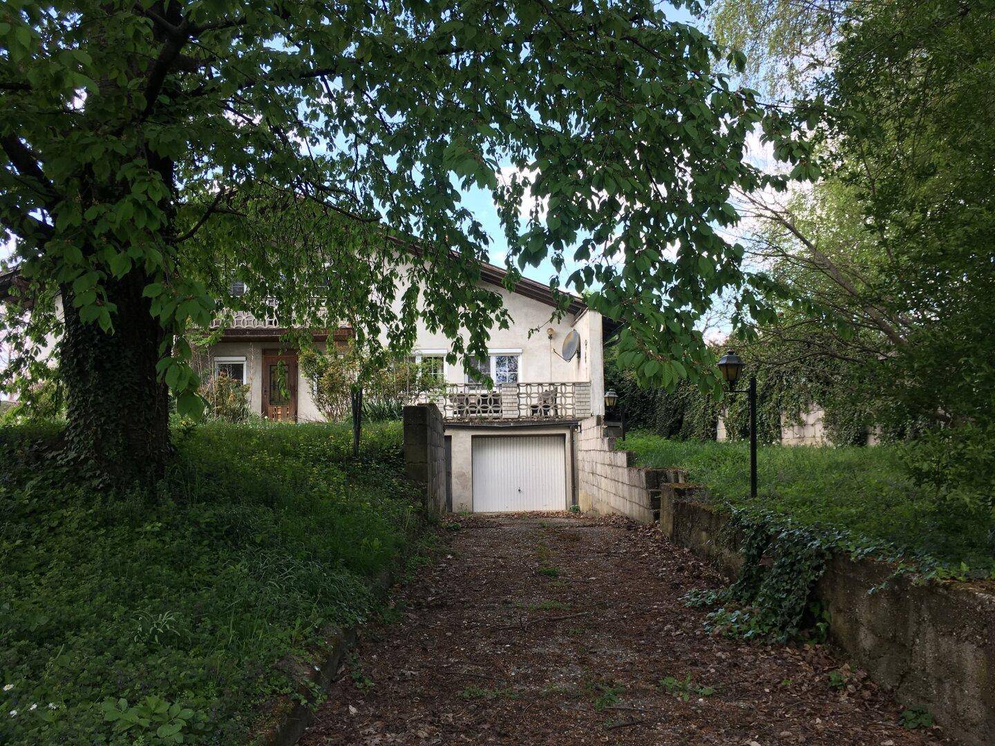 Wohnhaus mit integrierter Garage im Untergeschoss und einem kleinen Balkon, umgeben von Bäumen.