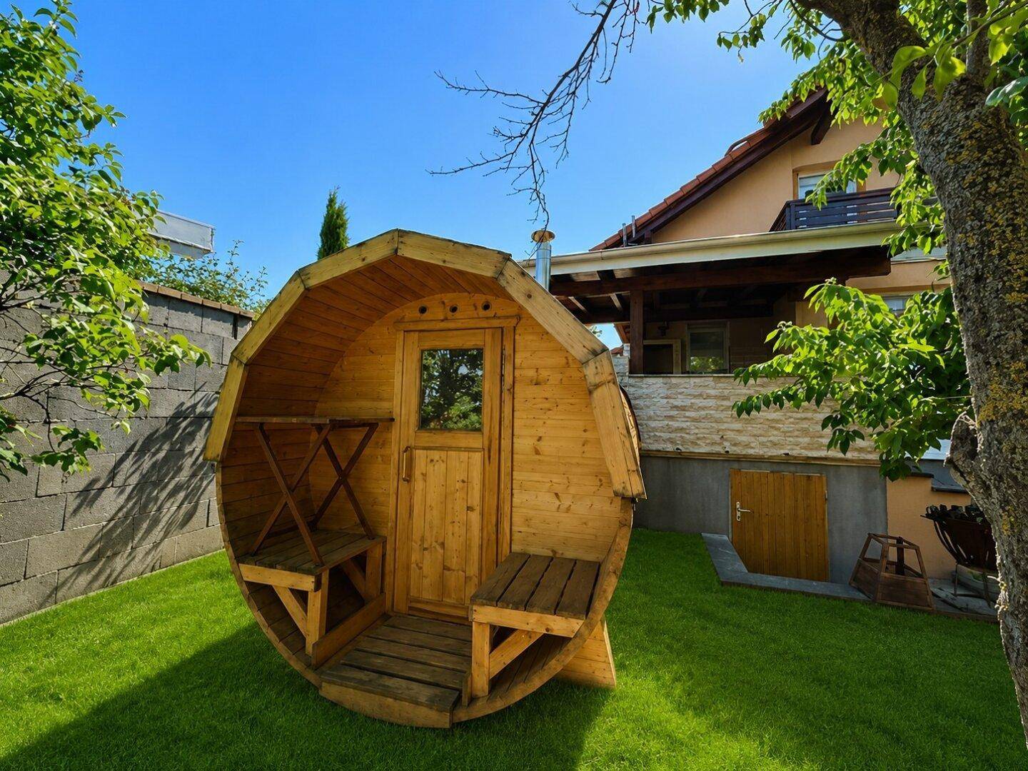 Gartenbereich mit einer freistehenden Fasssauna und viel Grünfläche.