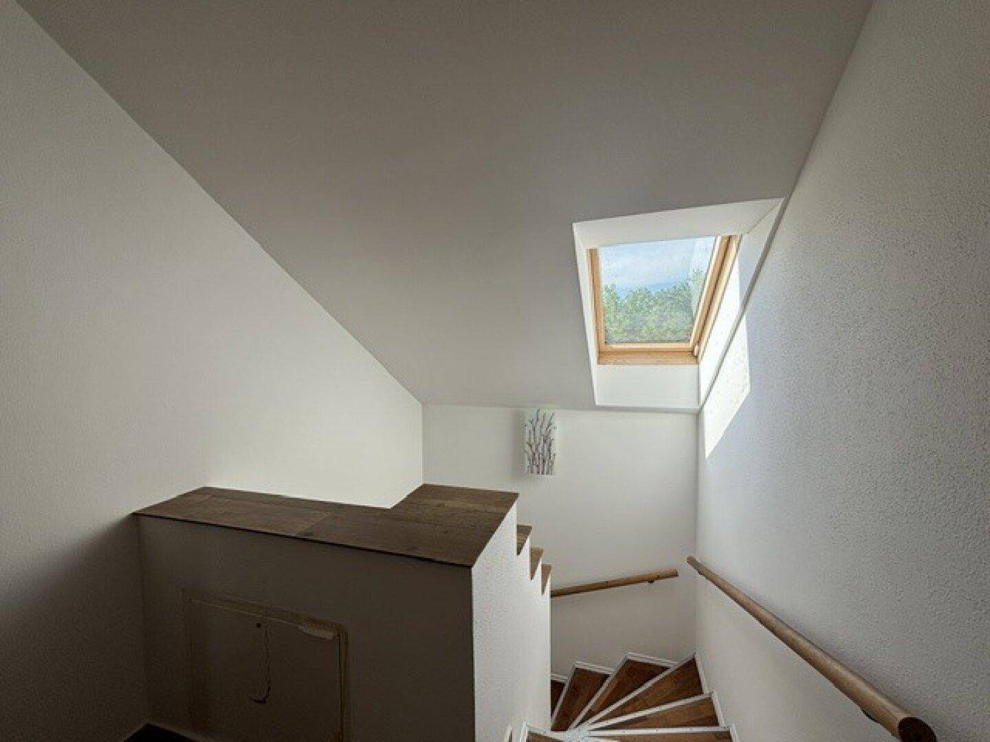 Heller Treppenaufgang mit Holzstufen und einem Dachfenster, das viel Licht spendet.
