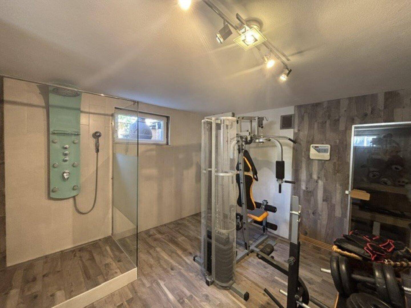 Fitnessraum im Untergeschoss mit Trainingsgeräten und integrierter Duschkabine.