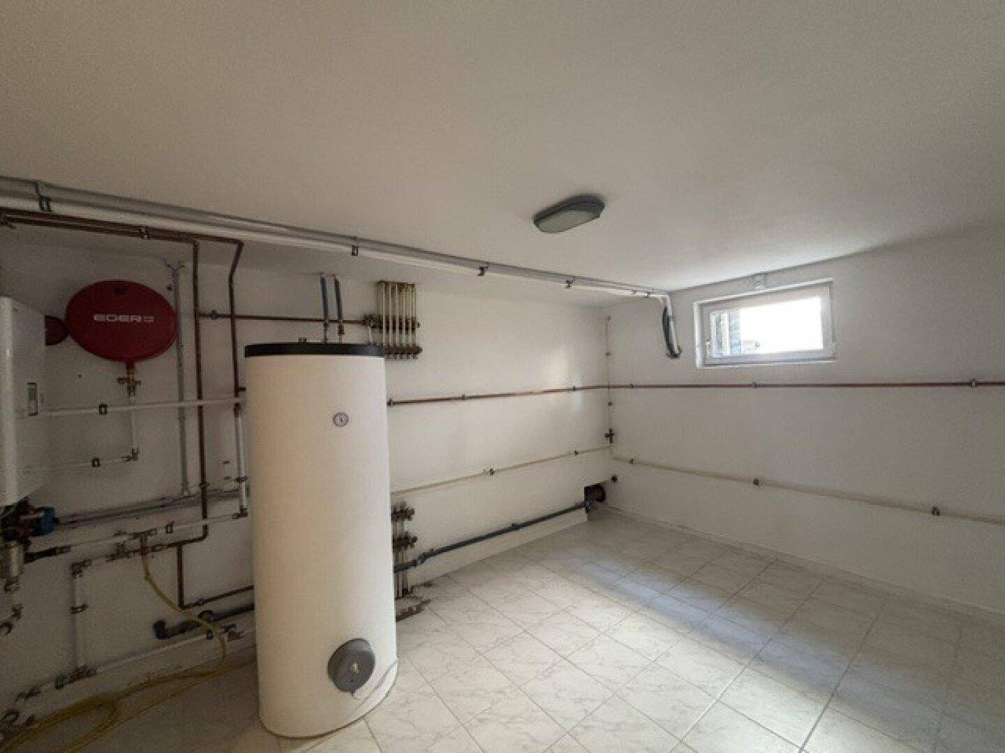Technikraum im Untergeschoss mit Warmwasserspeicher und sichtbaren Installationen.