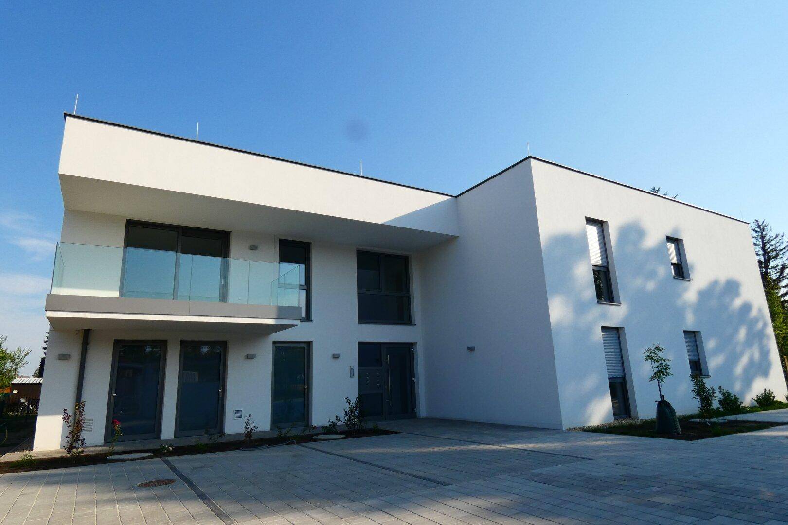 Frontansicht des modernen Neubaus mit klaren Linien, Glasbalkonen und großzügigen Parkflächen.