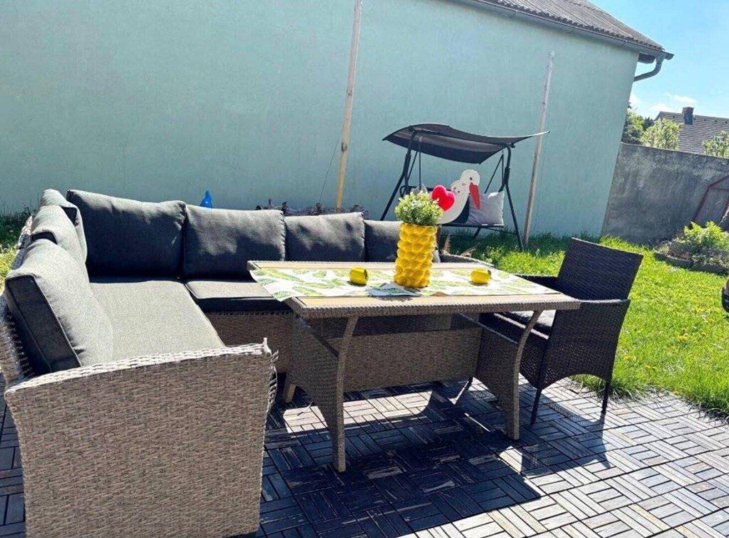 Entspannungsbereich auf der Terrasse mit bequemen Gartenmöbeln und einer Schaukel im Hintergrund.