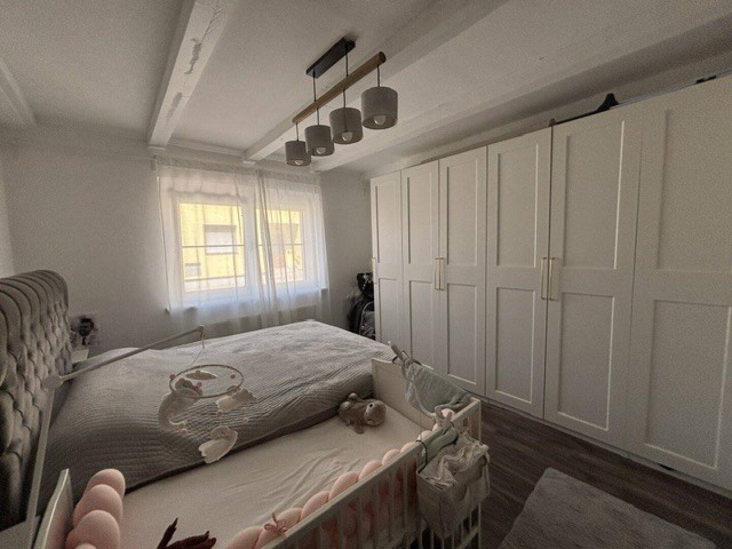 Helles Schlafzimmer mit großem Bett, Babybett und praktischen Einbauschränken sowie sichtbaren Deckenbalken.
