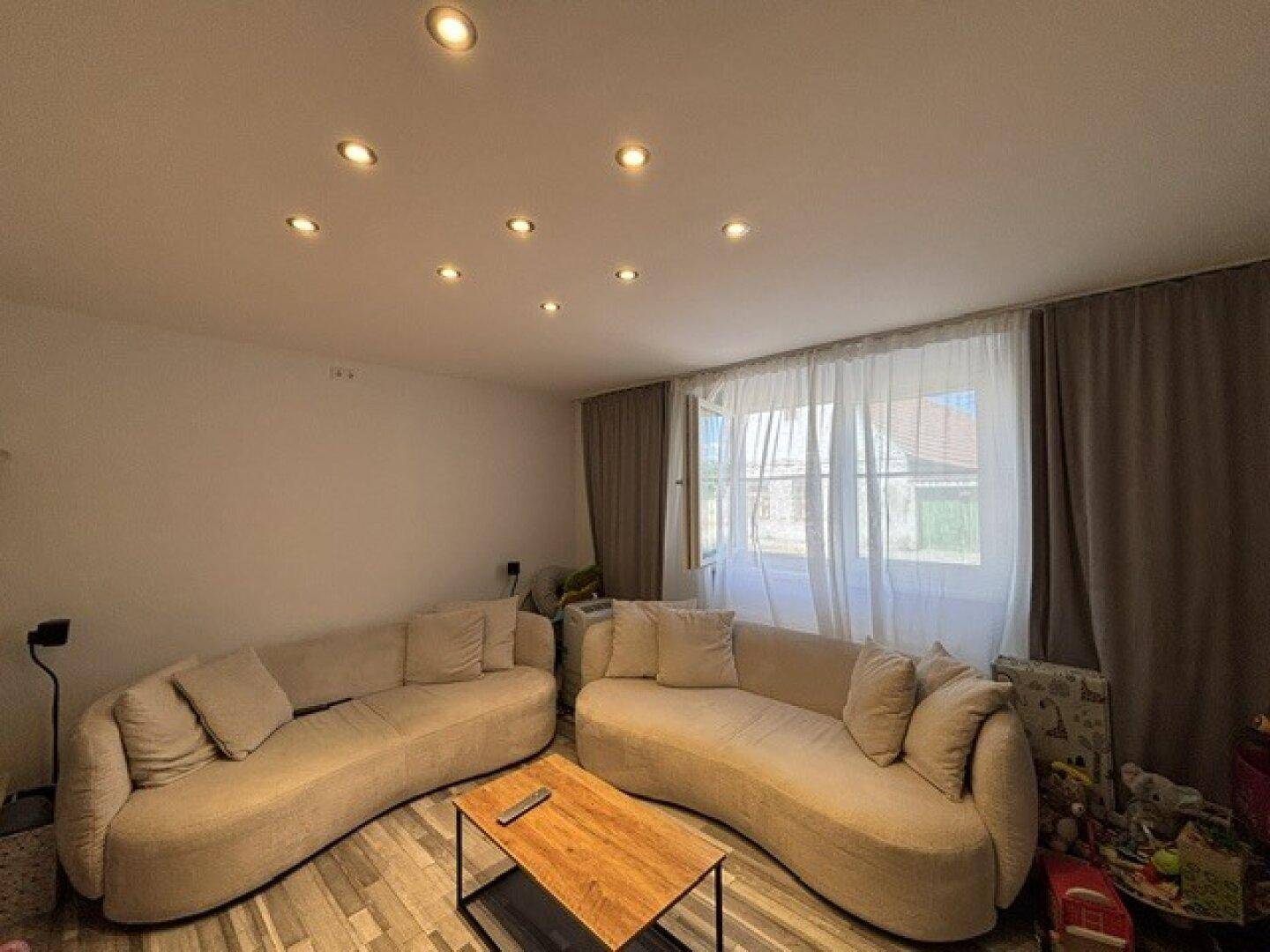 Helles Wohnzimmer mit zwei modernen Sofas, Couchtisch und Deckenstrahlern, durchflutet von Tageslicht.