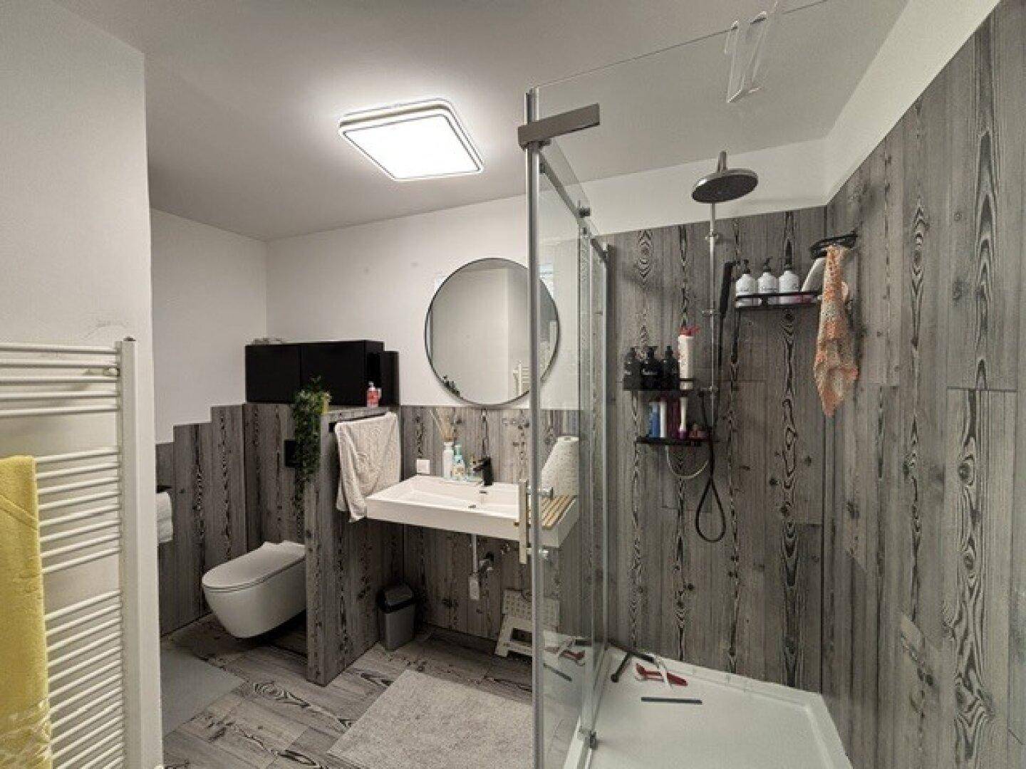 Modernes Badezimmer mit ebenerdiger Dusche, wandhängendem WC und Holzoptik-Wandverkleidung.