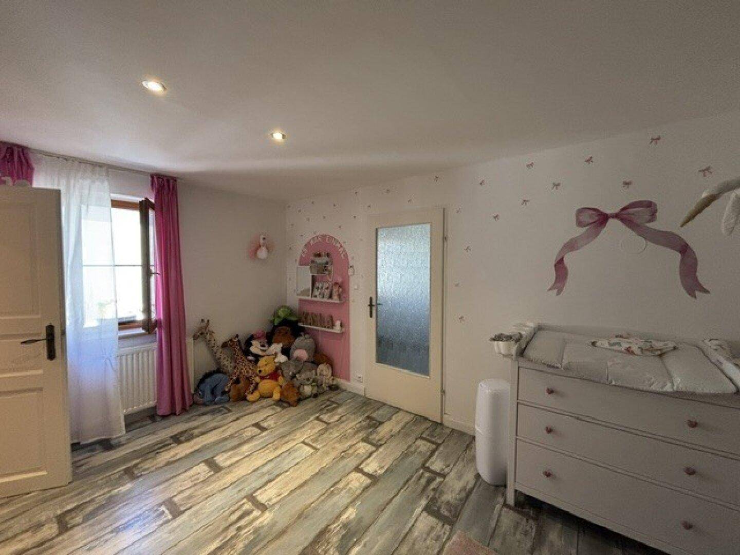 Freundliches Kinderzimmer mit Wickeltisch, vielen Stofftieren und einem verspielten Wanddesign.
