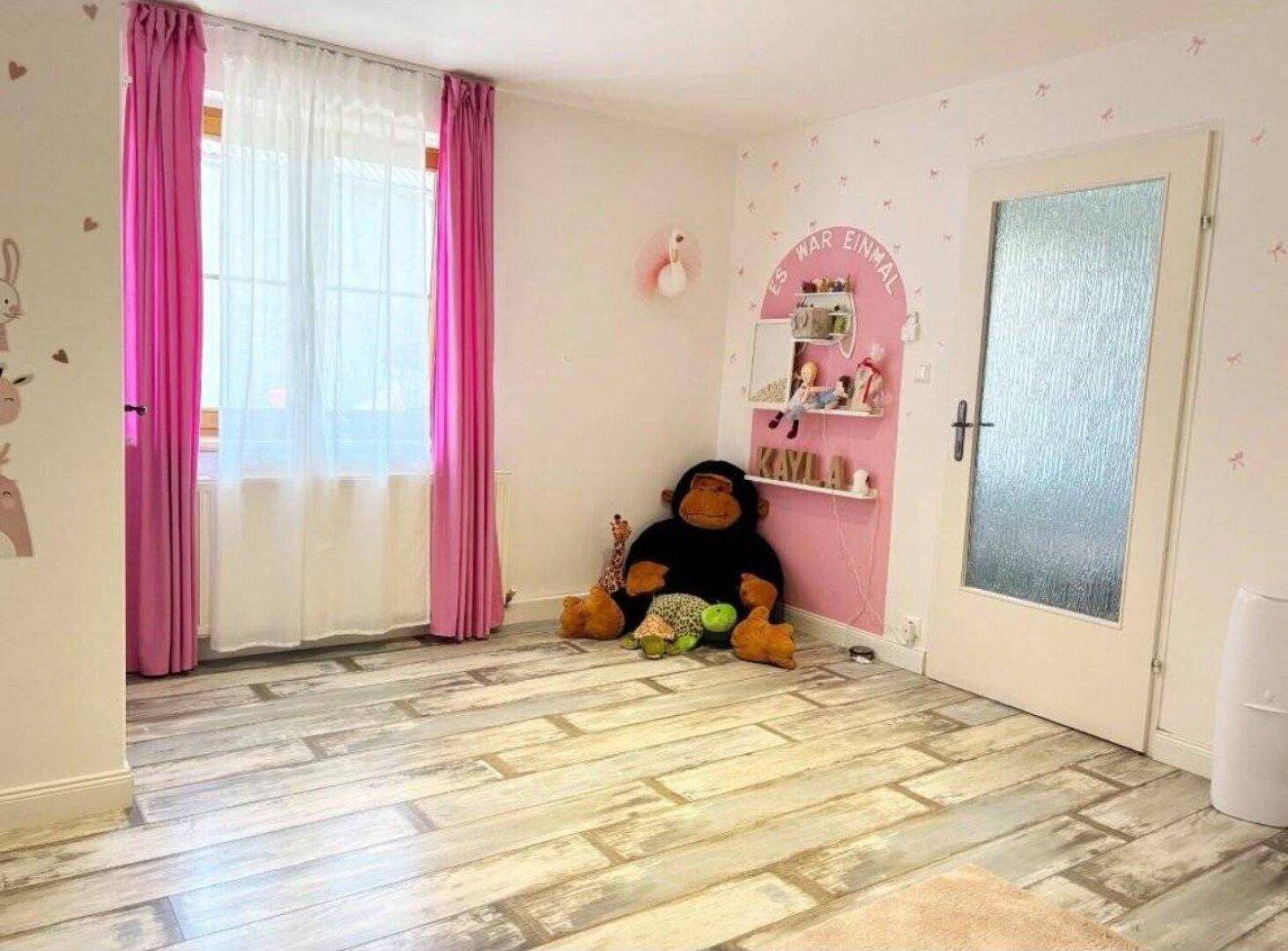 Charmantes Kinderzimmer mit rosa Vorhängen, großen Stofftieren und verspielten Wanddekorationen.