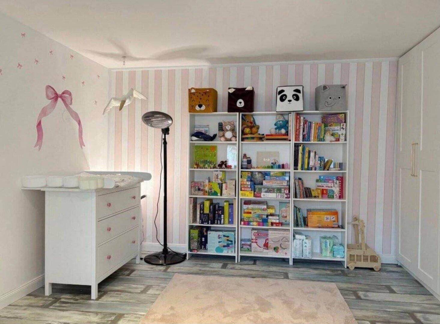 Helles Kinderzimmer mit Wickeltisch, Bücherregalen und gestreifter Tapete, ideal für kleine Kinder.