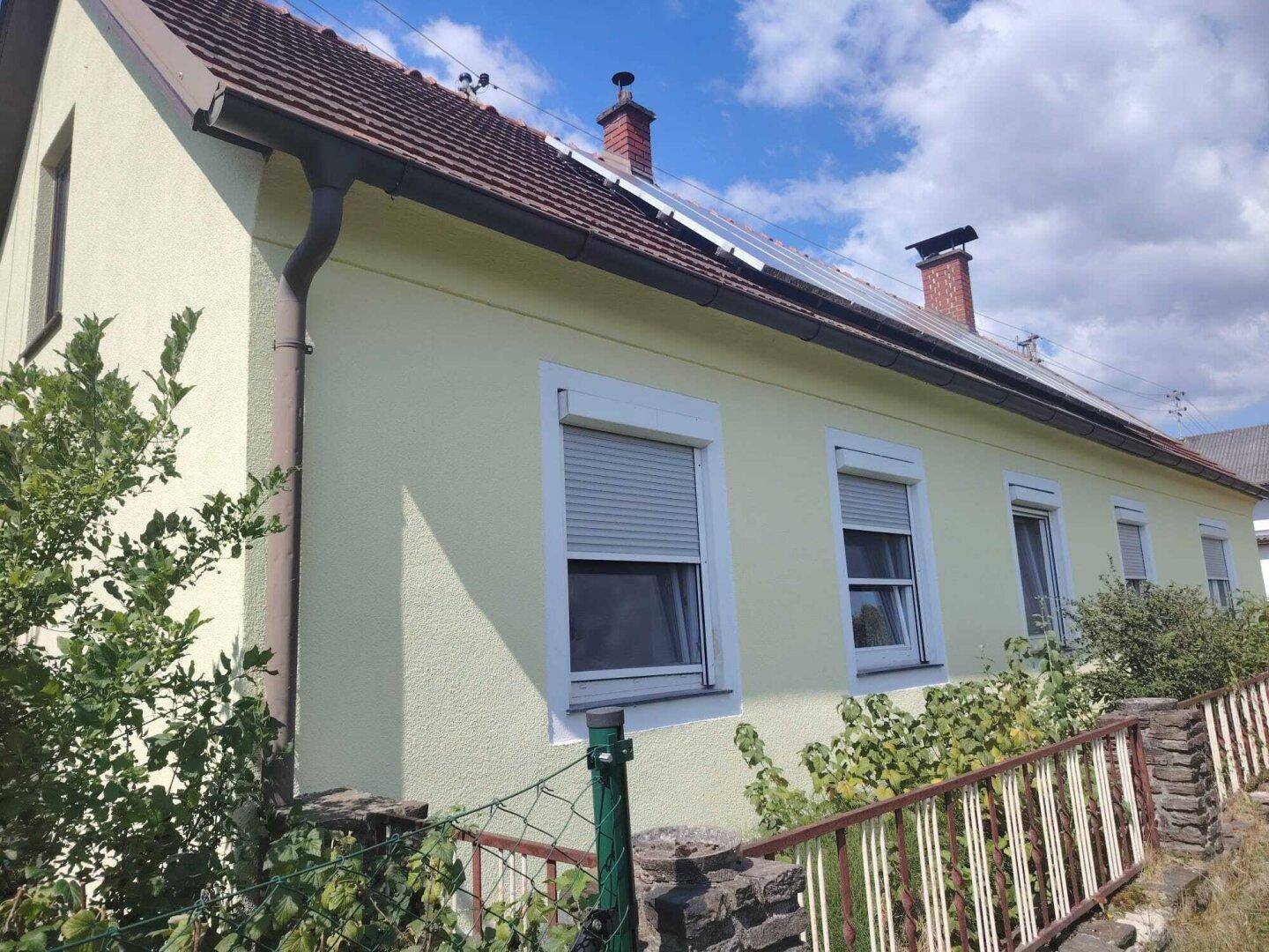 Nahaufnahme der Hausfassade mit gelbem Putz, Rollläden und Dachrinne.