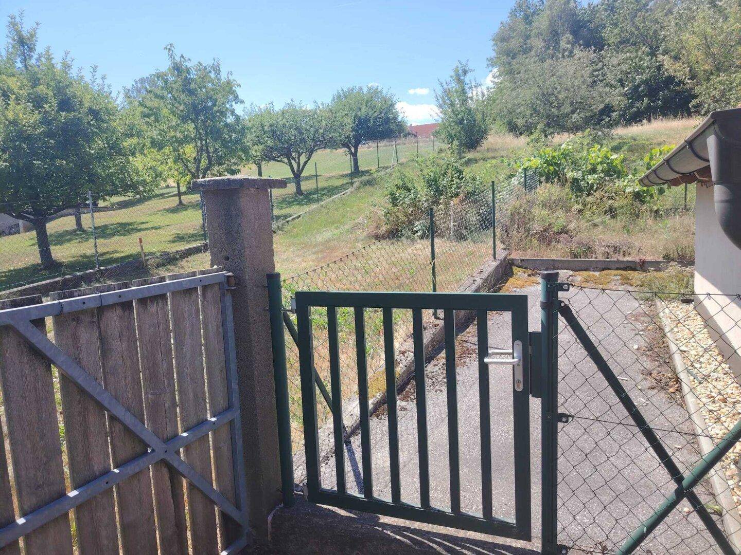 Grünes Gartentor führt zu einem weitläufigen Garten mit Obstbäumen und Hügellandschaft.