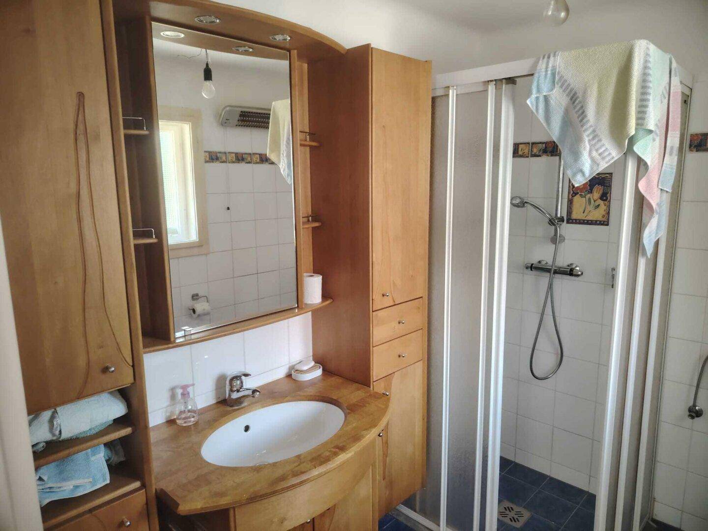 Helles Badezimmer mit Holzmöbeln, Waschbecken und Duschkabine.