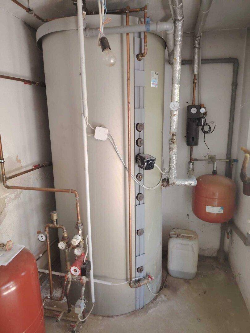 Technikraum mit großem Warmwasserspeicher und sichtbaren Rohrleitungen.