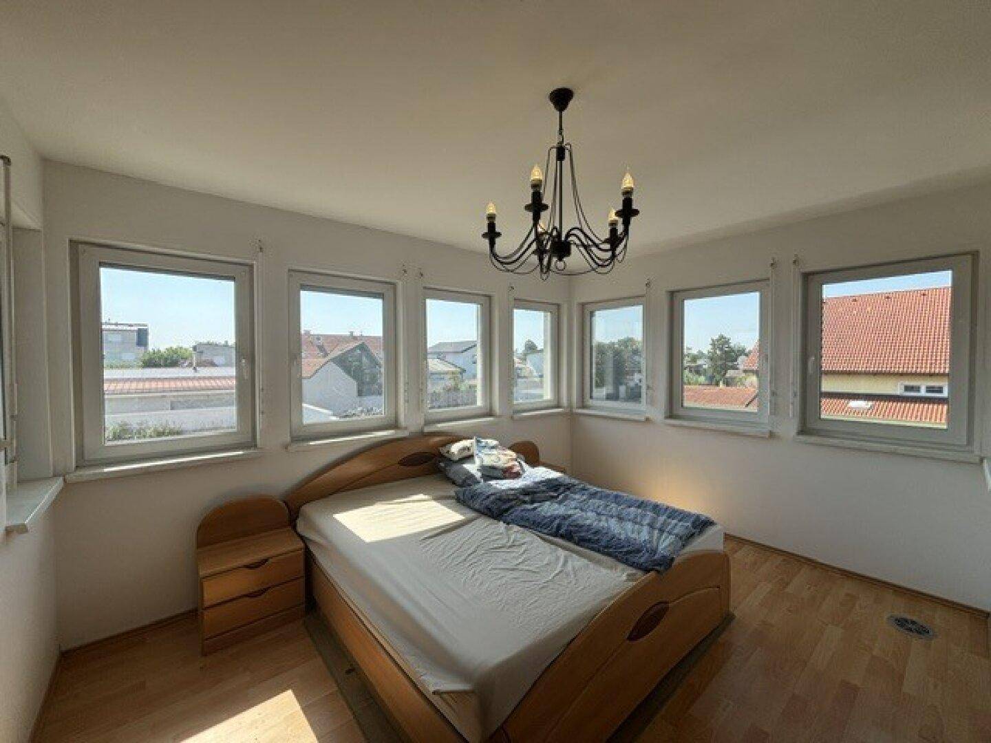Schlafzimmer mit vielen Fenstern, Holzbett und Blick auf die Umgebung.