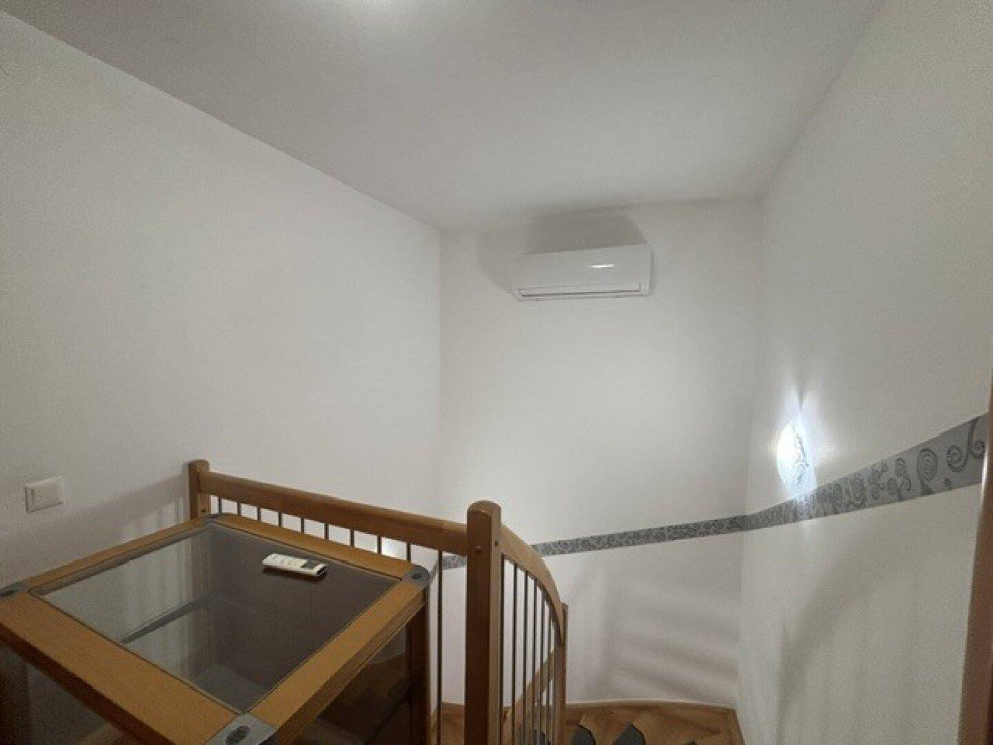 Treppenhaus mit Holzgeländer und installierter Klimaanlage an der Wand.