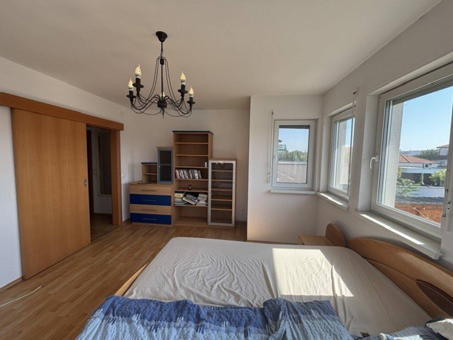 Helles Schlafzimmer mit Laminatboden, Schiebetür und Blick nach draußen.