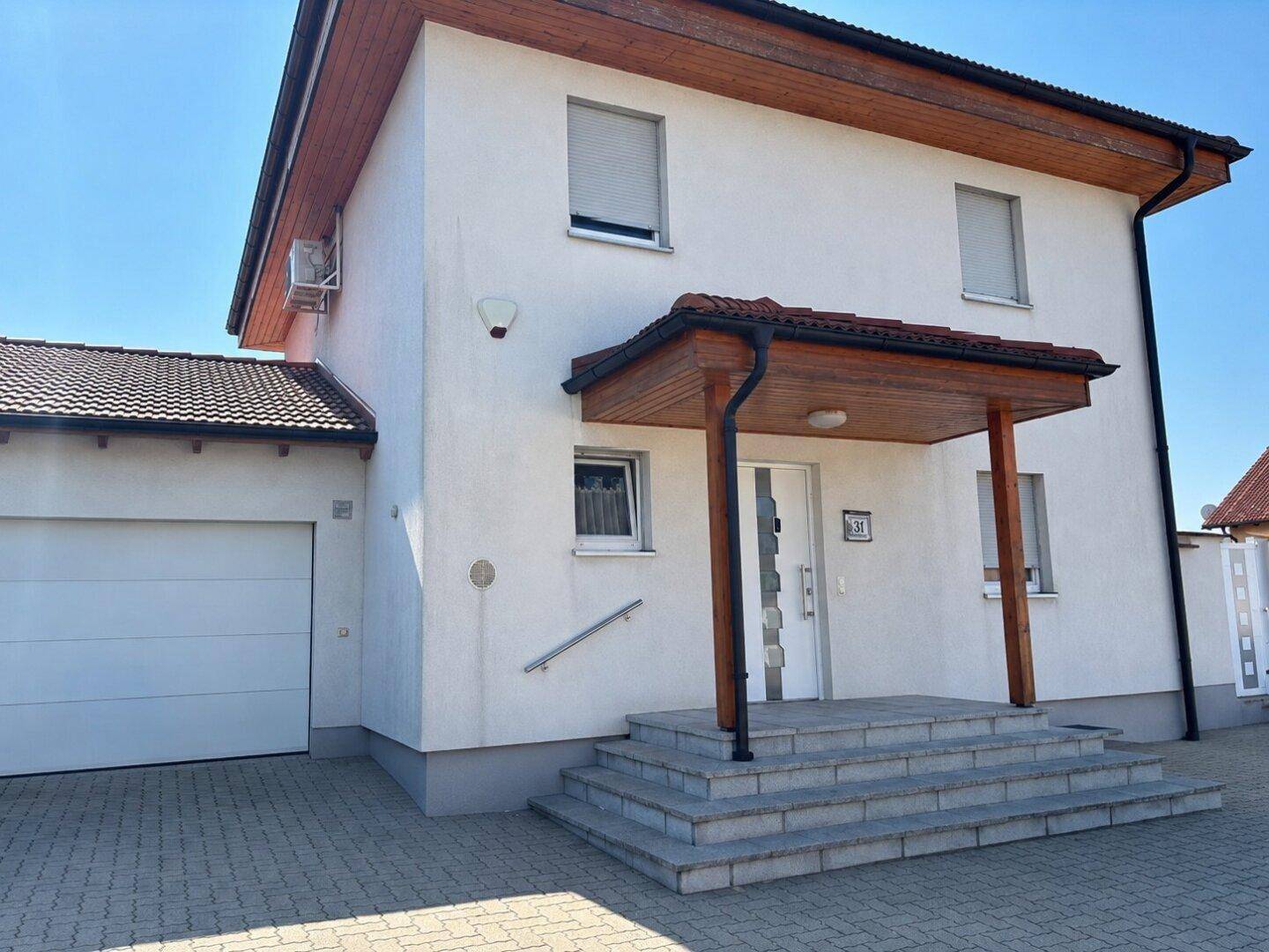 Weißes Einfamilienhaus mit gepflastertem Vorplatz, Garage und überdachtem Eingangsbereich.