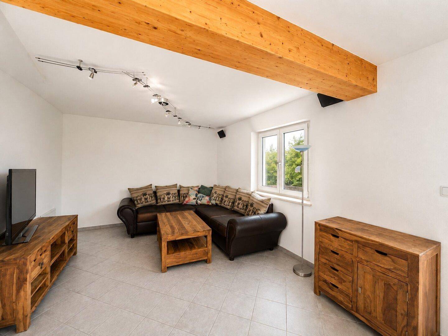 Gemütliches Wohnzimmer mit Holzbalken, Fliesenboden und bequemer Ledercouch.