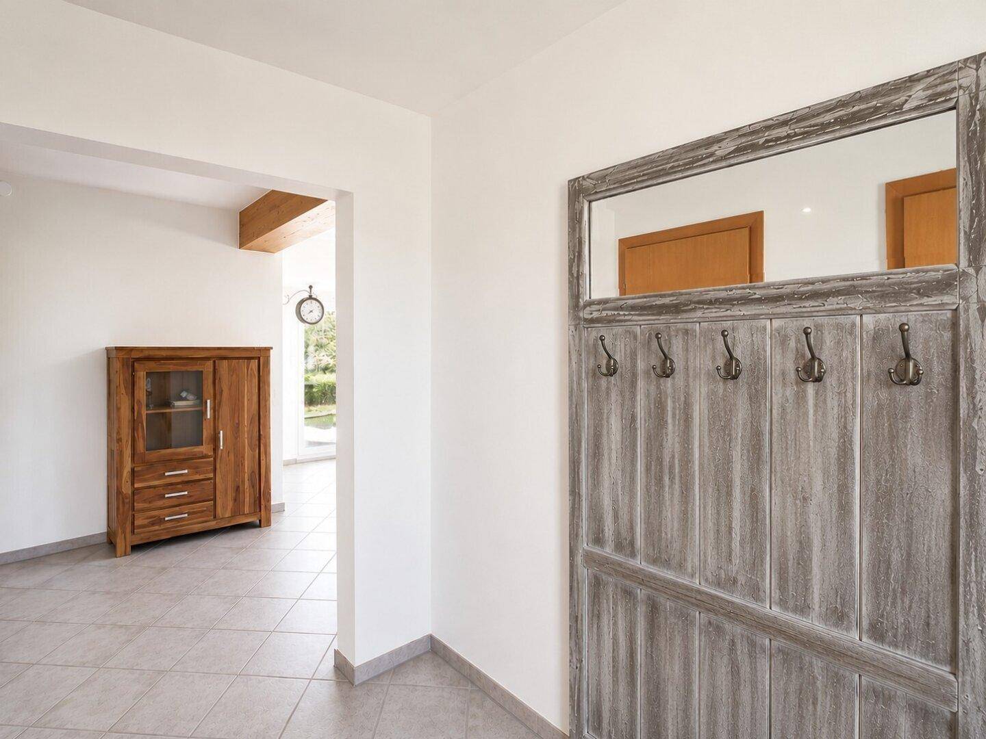 Heller Flur mit Fliesenboden und rustikaler Garderobe mit Spiegel.