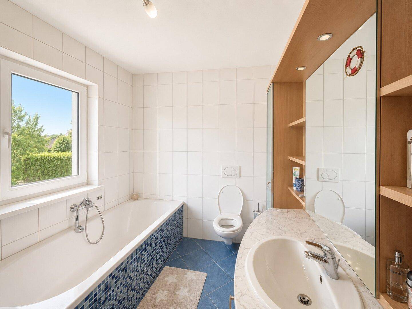 Helles Badezimmer mit Badewanne, WC, großem Spiegel und Fenster.