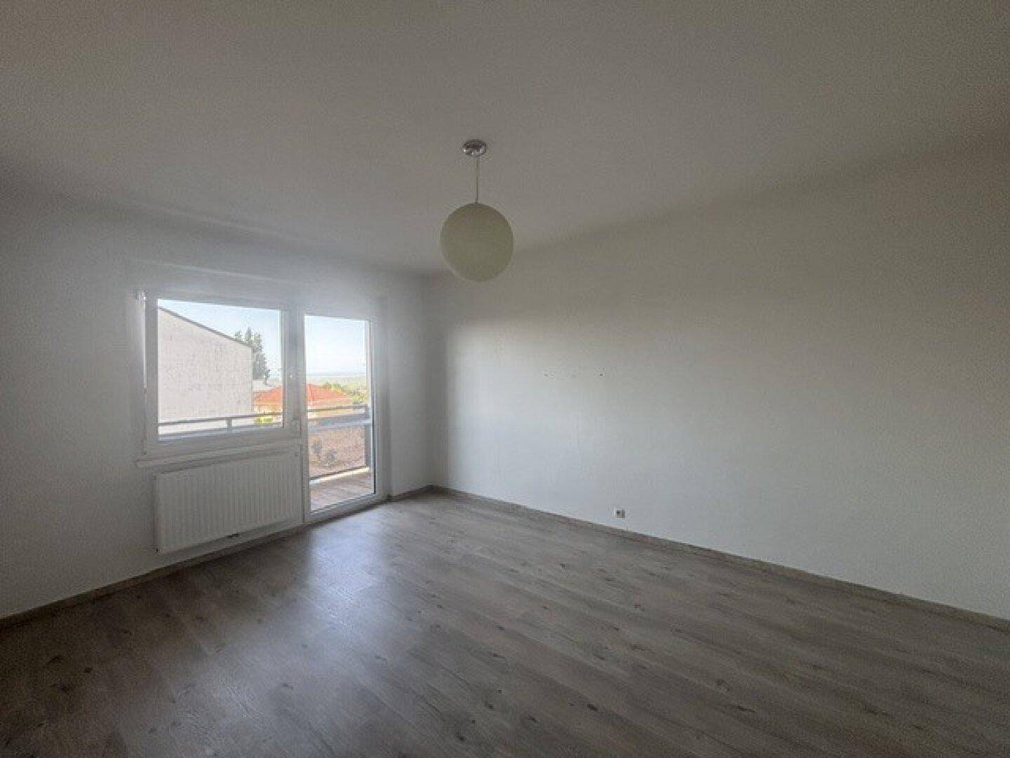 Heller Raum mit Laminatboden und großem Fenster mit Zugang zu einem Außenbereich.