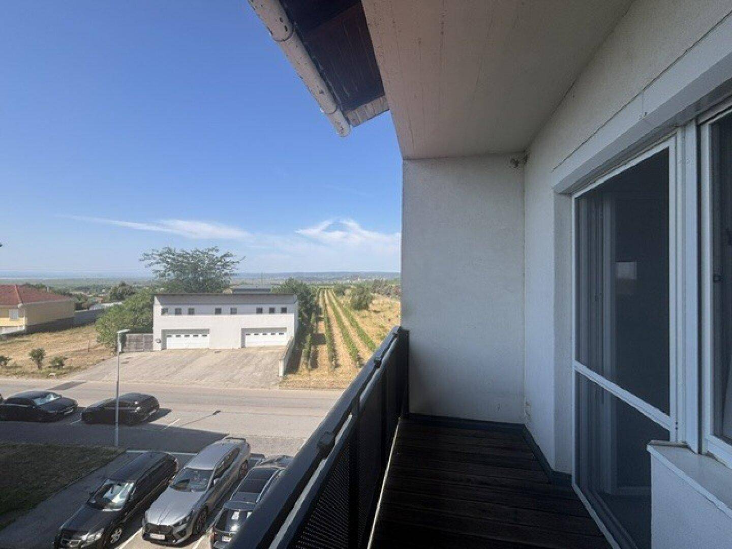 Balkon mit weitem Blick über einen Parkplatz, ein Gebäude und die umliegenden Weinberge.