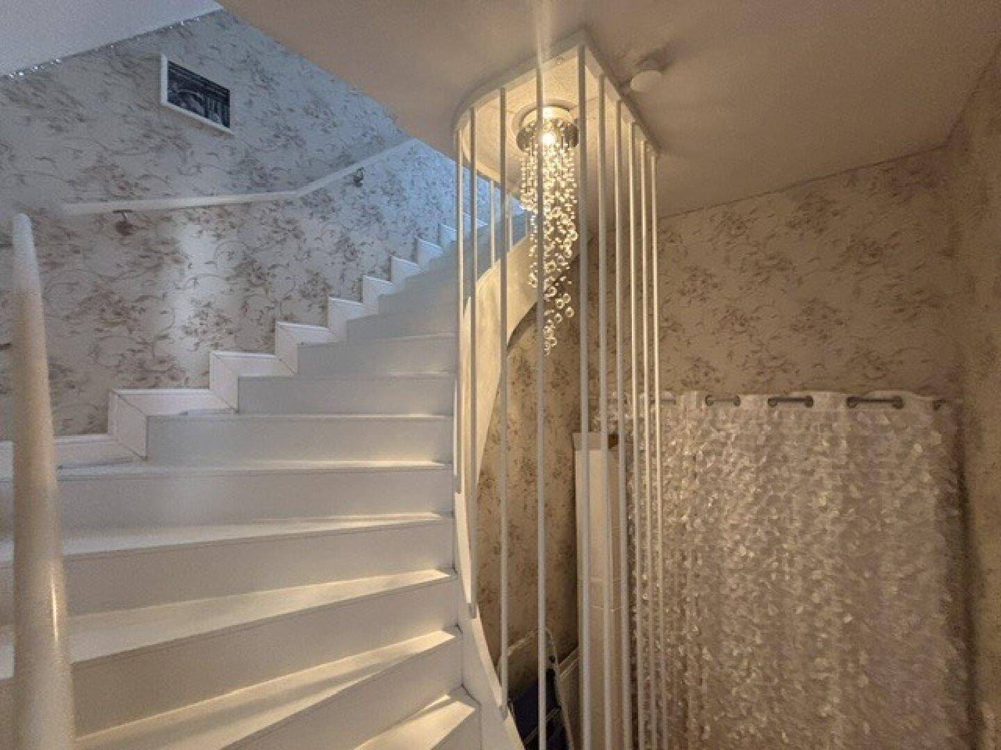 Heller Treppenaufgang mit weißer Treppe und einem dekorativen Kronleuchter.
