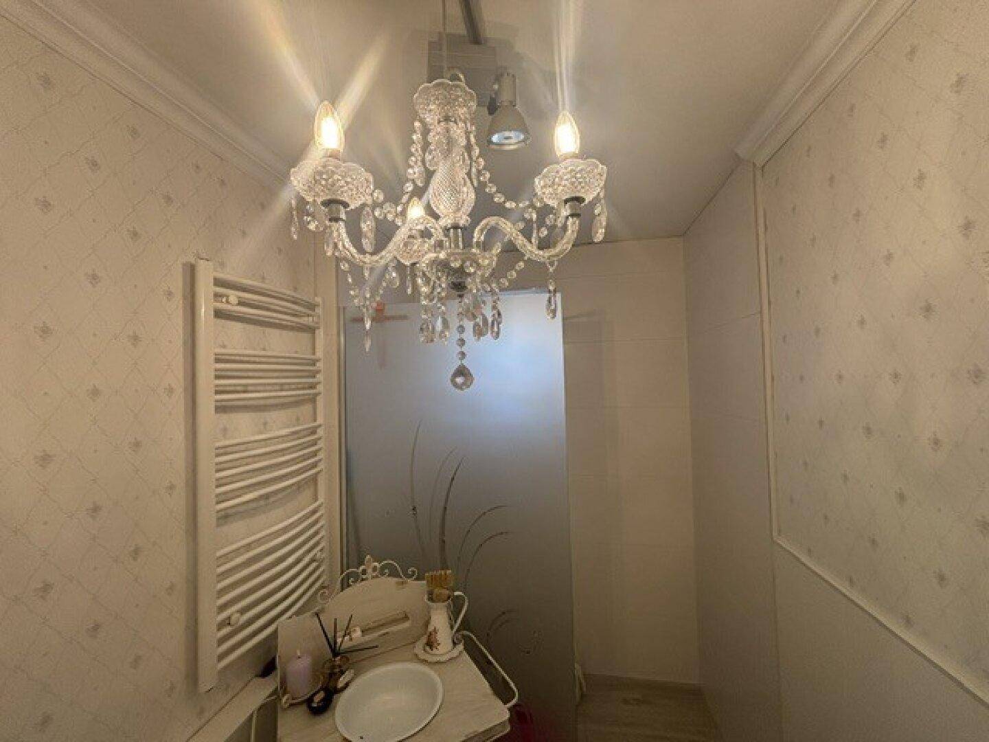 Kleines Badezimmer mit Kristallleuchter, beheiztem Handtuchhalter und dekorativer Tapete.