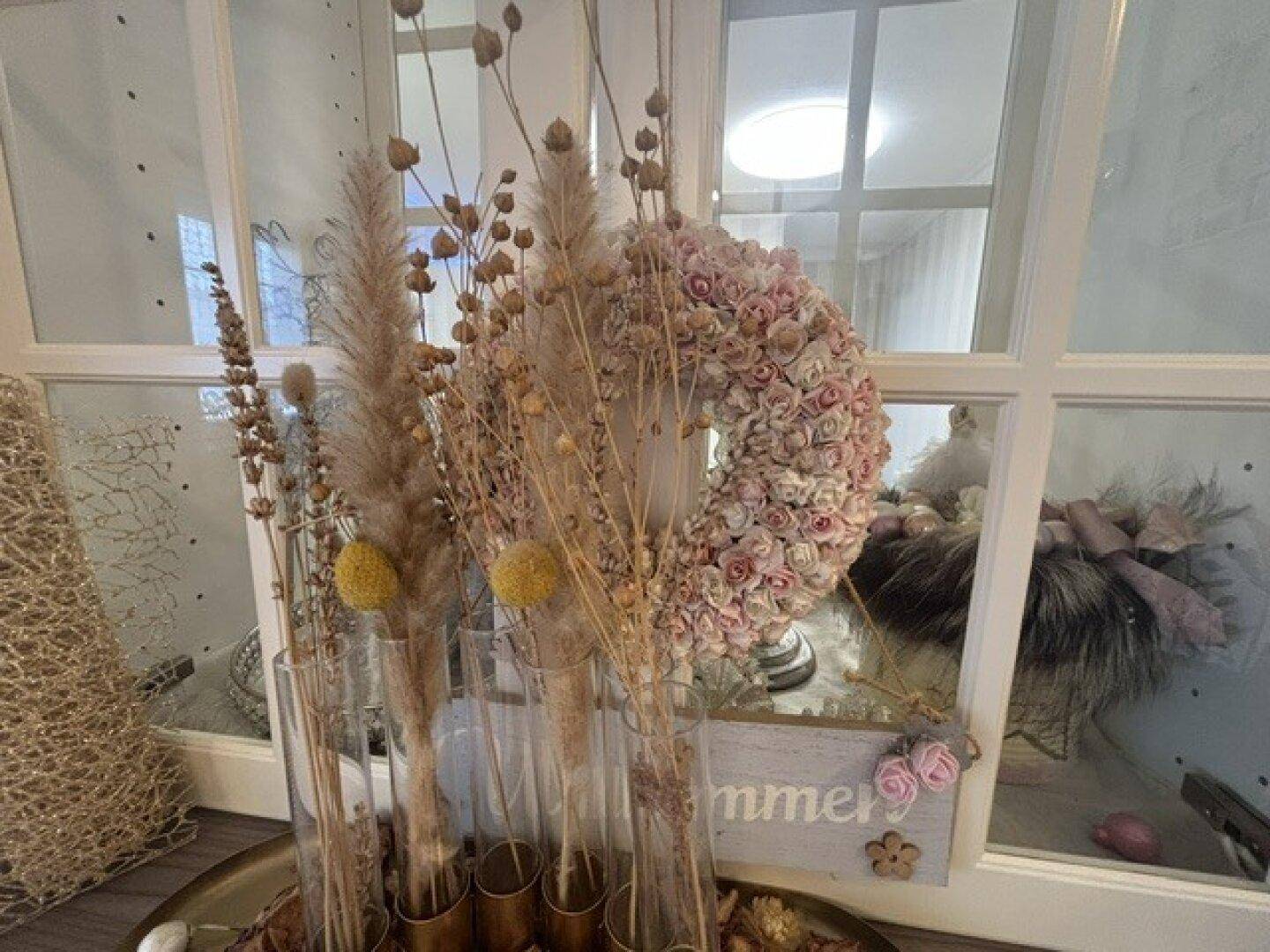 Dekorative Fensterbank mit Trockenblumen und einem Kranz, der durch das Fenster sichtbar ist.