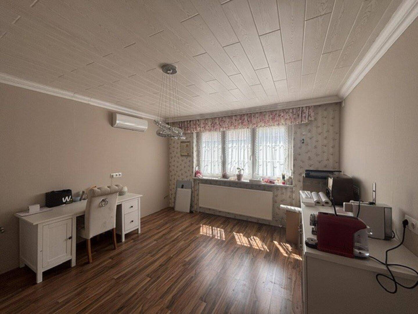 Helles Zimmer mit Holzboden, Schreibtisch und Klimaanlage an der Wand.