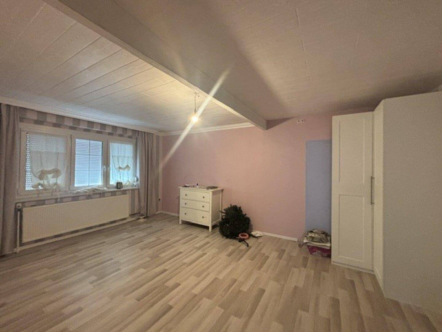 Schlafzimmer mit hellem Holzboden, rosa Wänden und einem Kleiderschrank.
