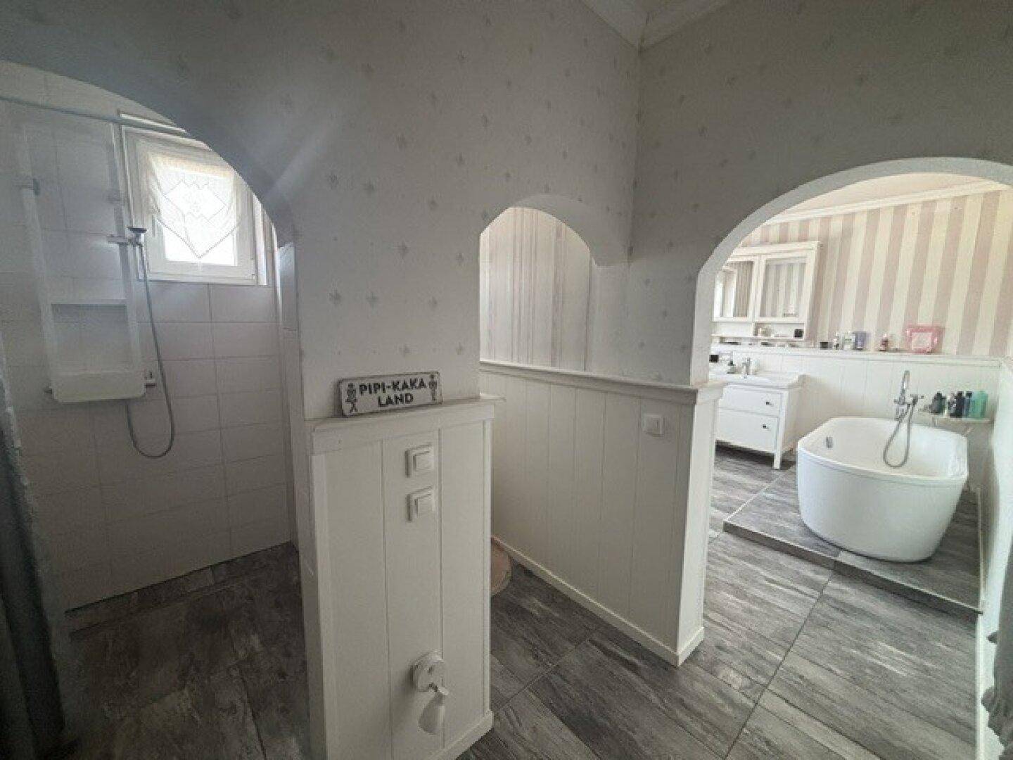 Geräumiges Badezimmer mit freistehender Badewanne, Duschbereich und Holzboden.