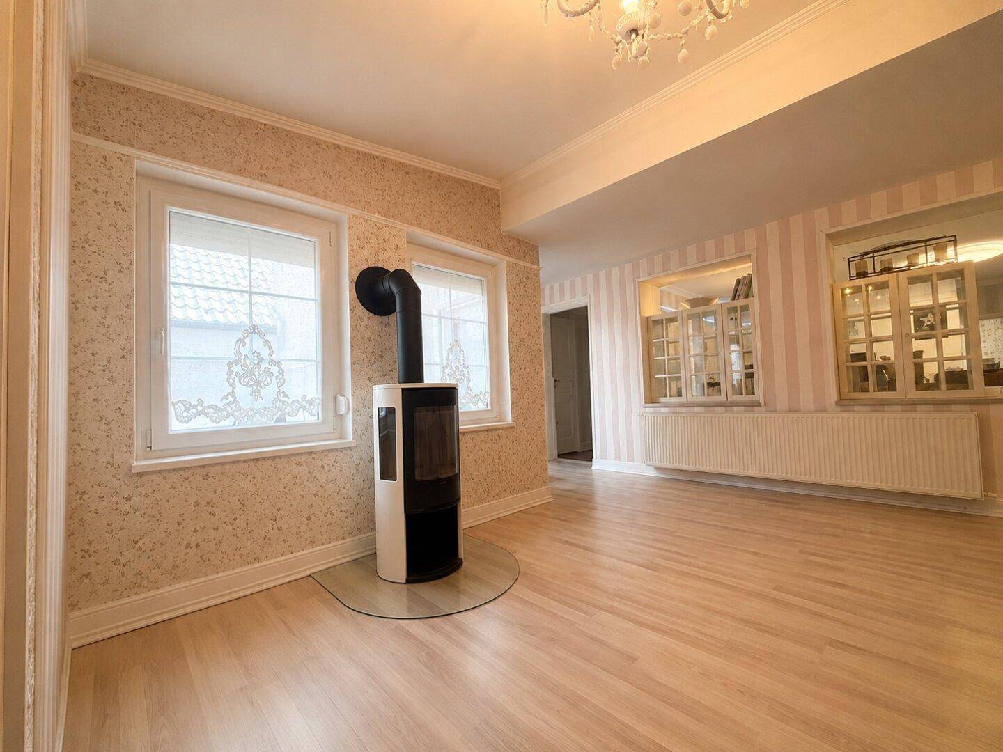Geräumiges Wohnzimmer mit Kaminofen, hellem Holzboden und großen Fenstern.