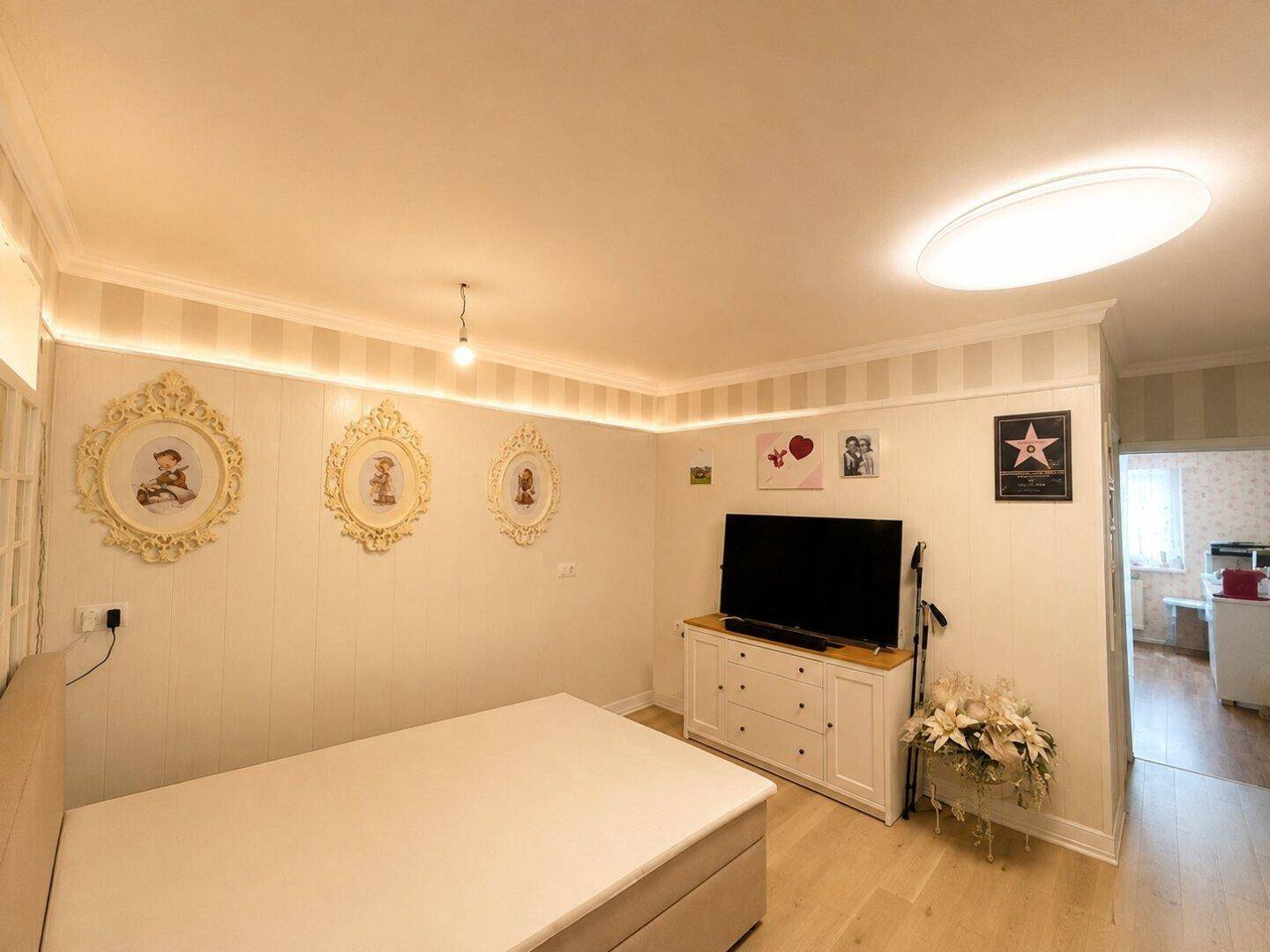 Gemütliches Schlafzimmer mit hellem Holzboden, indirekter Beleuchtung und dekorativen Wandbildern.