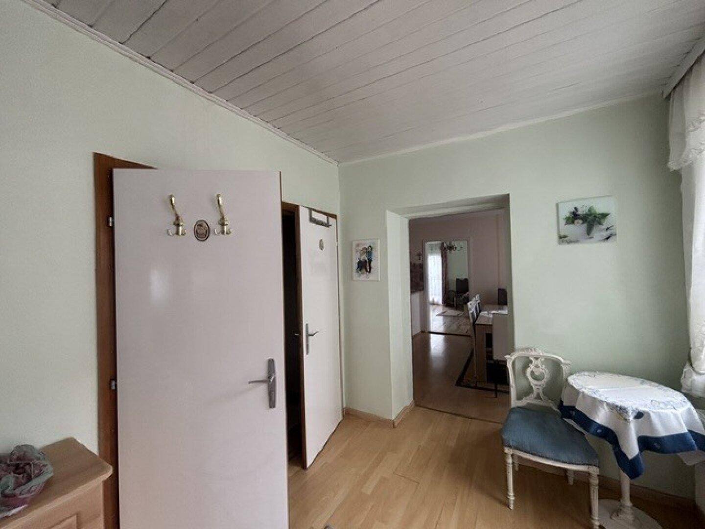 Flur mit Holzdecke, hellgrünen Wänden und einem kleinen Tisch mit Stuhl.
