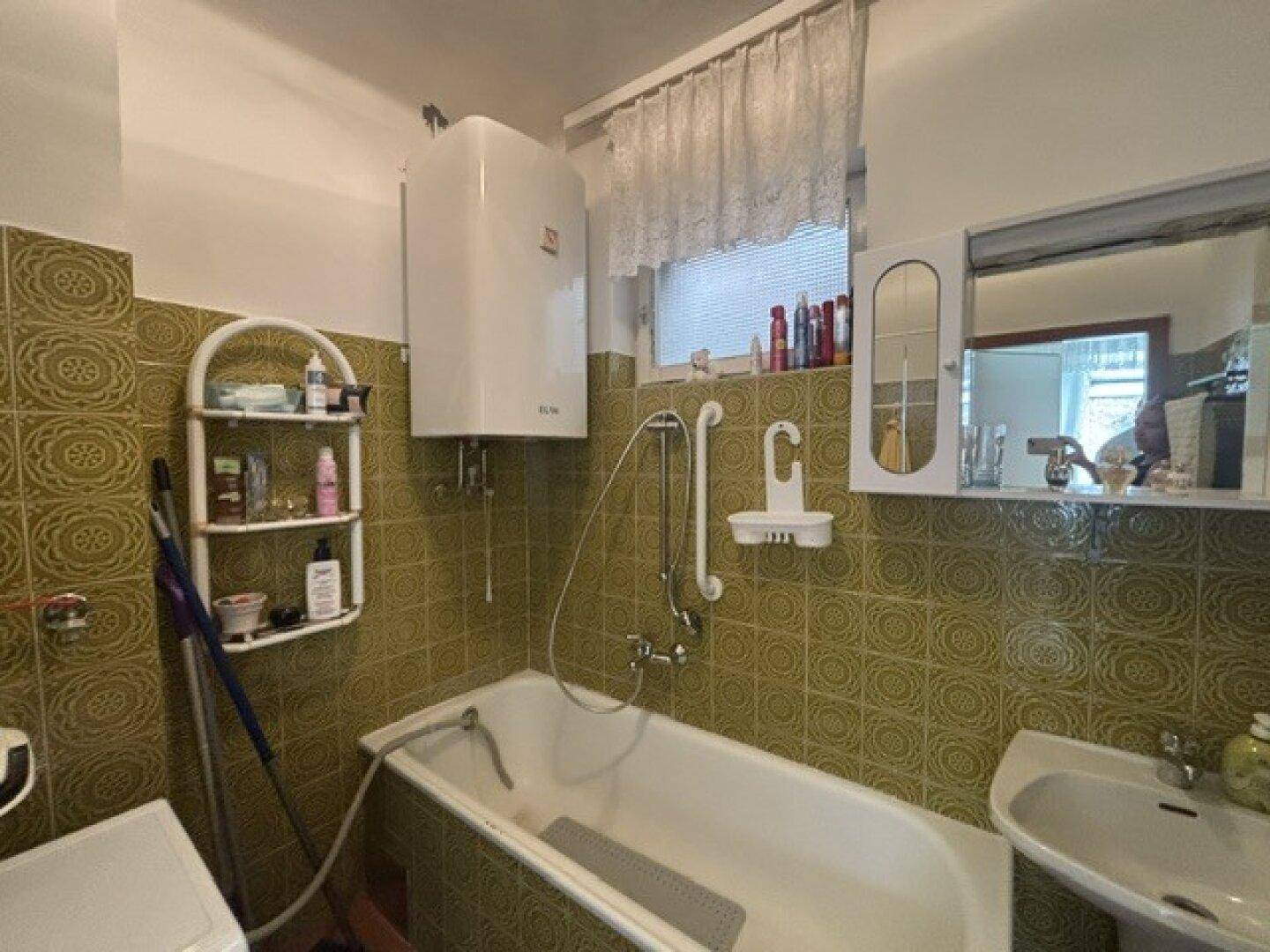 Badezimmer mit Badewanne, Waschbecken, Spiegelschrank und grünen Fliesen im Retro-Stil.