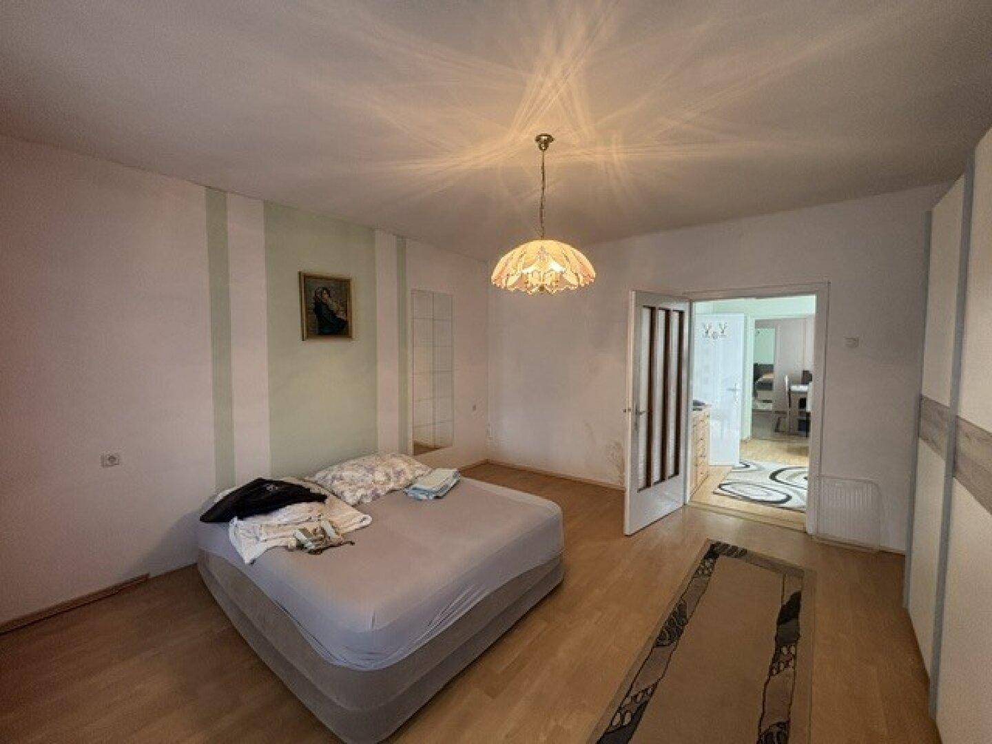 Schlafzimmer mit Holzboden und offener Tür, die zu einem weiteren Raum führt.