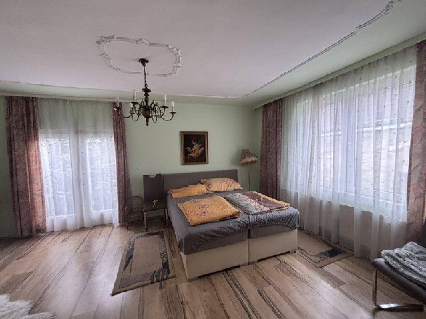 Schlafzimmer mit Doppelbett, Holzboden und einer Stuckdecke mit Kronleuchter.